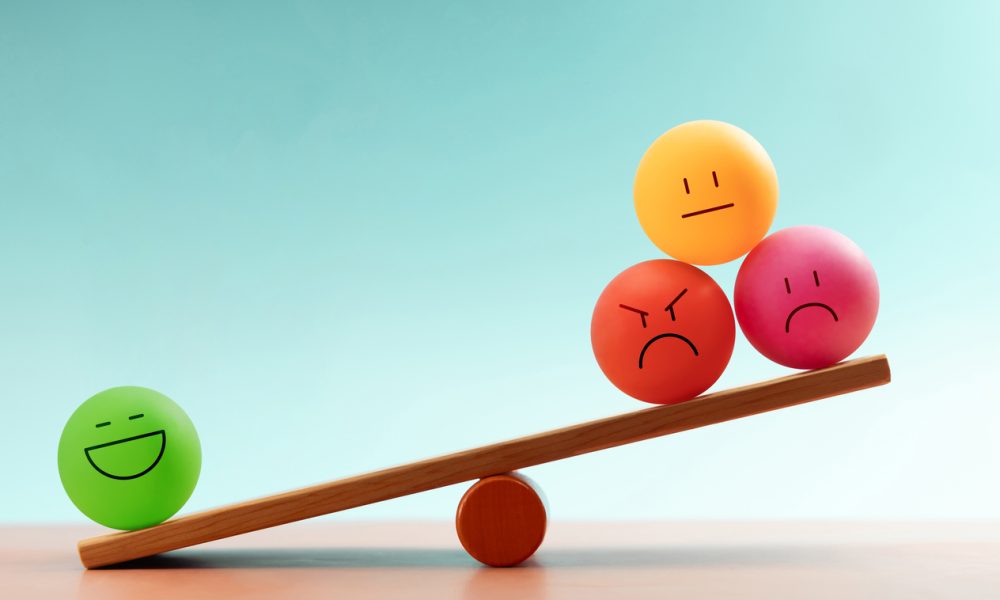 Colorful emotional faces balancing on a seesaw, symbolizing mental health and emotional self-regulation through balancing positive and negative emotions